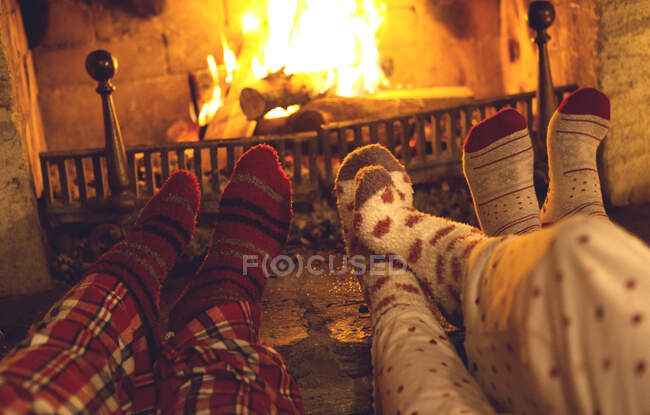 Piernas y pies de tres personas con pijamas y calcetines calientes tumbados frente a una chimenea. - foto de stock