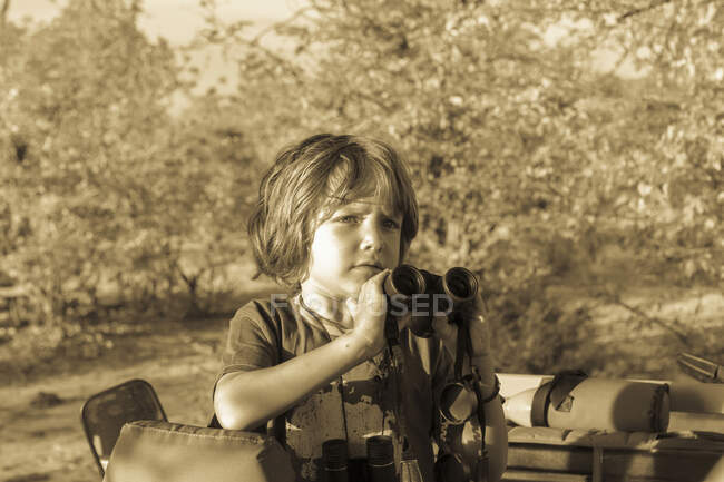 Ein fünfjähriger Junge mit einem Fernglas steht in einem offenen Fahrzeug im Wald. — Stockfoto