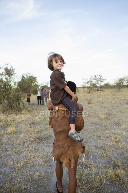 Пятилетний мальчик едет на плечах Сан-Бушмена. — стоковое фото