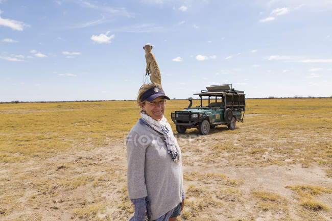 Mujer adulta con suricata en la cabeza, desierto de Kalahari, sartenes Makgadikgadi, Botswana - foto de stock