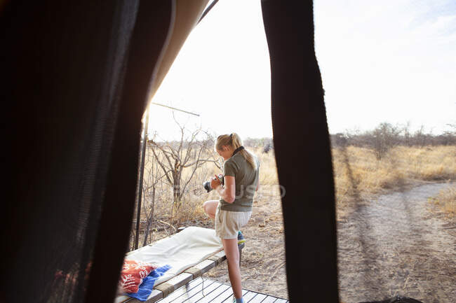 Una niña de doce años parada frente a una tienda de campaña en un campamento de reserva de vida silvestre, usando su cámara. - foto de stock