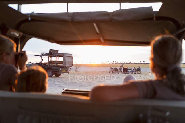 Family in safari vehicle taking photographs of a safari picnic at sunset. — Stock Photo