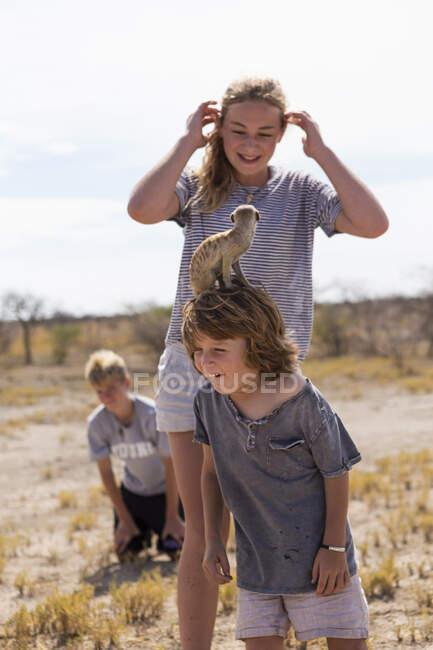 5-летний мальчик с сурикатом на голове, пустыня Калахари, соляные сковородки Макгадикгади, Ботсвана — стоковое фото