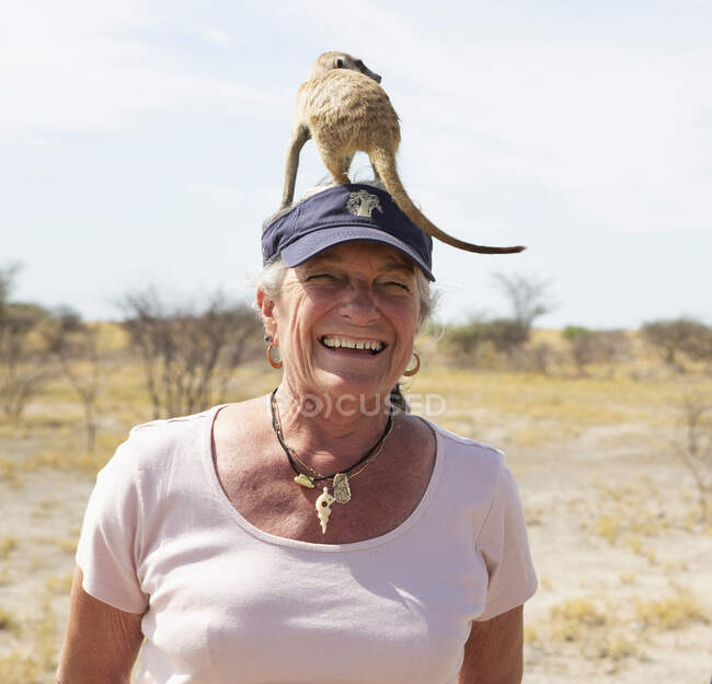 Улыбающаяся пожилая женщина с сурикатом на голове, пустыня Калахари, соляные сковородки Макгадикгади, Ботсвана — стоковое фото