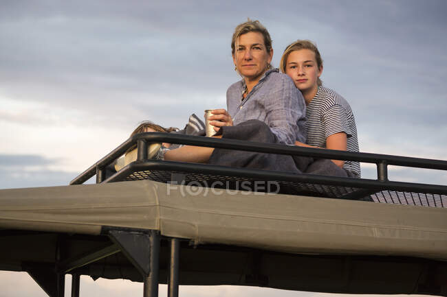 Madre e hija adolescente en la parte superior del vehículo safari mirando a la distancia. - foto de stock