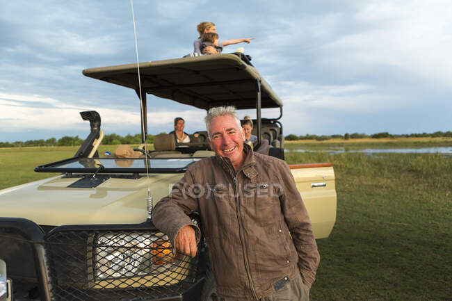 Um guia de safári sorridente e família de turistas em um veículo de safári. — Fotografia de Stock