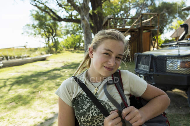 Ragazza di dodici anni con borse in un campo di riserva naturale, edifici e barche sullo sfondo. — Foto stock