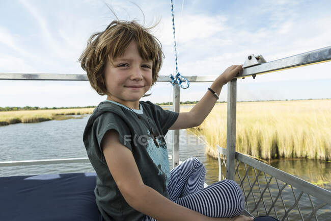 Um menino de cinco anos sentado em um barco na água. — Fotografia de Stock