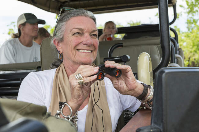 A family in a safari vehicle in a wildlife reserve, a senior woman with binoculars. — Stock Photo