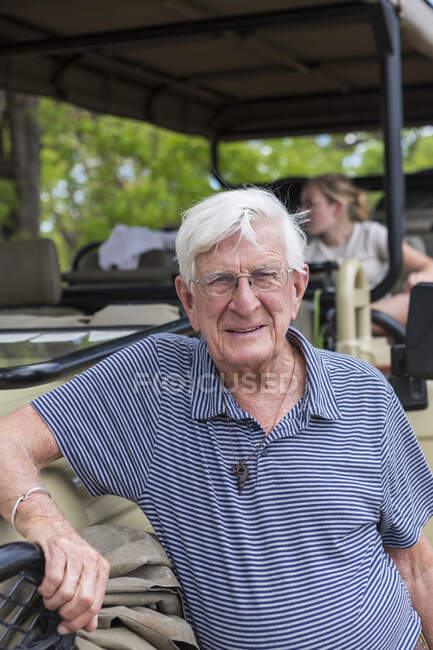 Старший мужчина, стоящий у машины сафари и улыбающийся в камеру — стоковое фото
