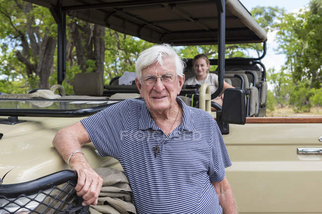 Hombre mayor de pie junto a un vehículo de safari y sonriendo a la cámara - foto de stock