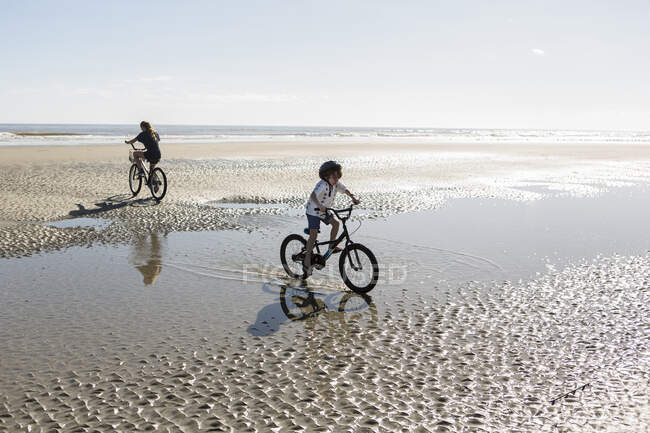 Duas crianças pedalando em uma praia aberta, um menino e uma menina. — Fotografia de Stock