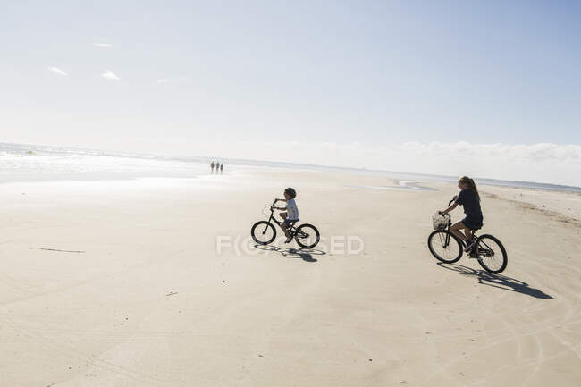 Duas crianças pedalando em uma praia aberta, um menino e uma menina. — Fotografia de Stock