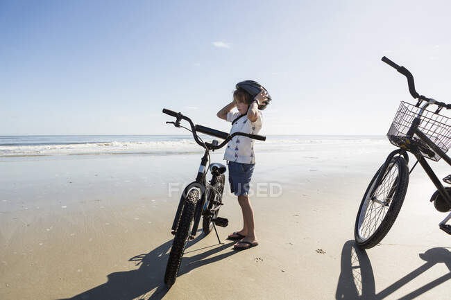 Un niño que se pone un casco de bicicleta en la playa, St. Simon 's Island, Georgia - foto de stock