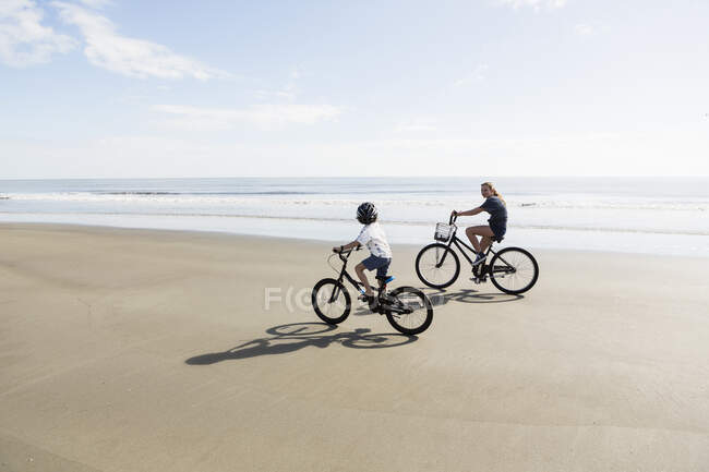Блудниці, хлопчик і дівчинка катаються на велосипеді на пляжі . — стокове фото