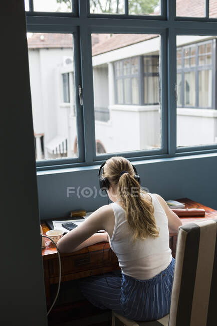 Тринадцятирічна дівчина в навушниках робить домашнє завдання, сидячи в тихому місці . — стокове фото