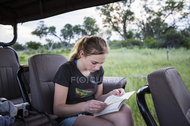 Niña de 13 años escribiendo en su diario sentada en un vehículo en safari - foto de stock