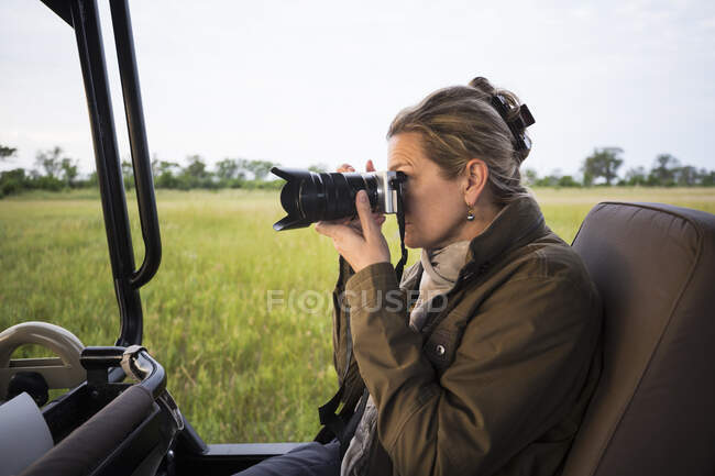Erwachsene Frau mit Kamera im Safari-Fahrzeug in freier Landschaft — Stockfoto