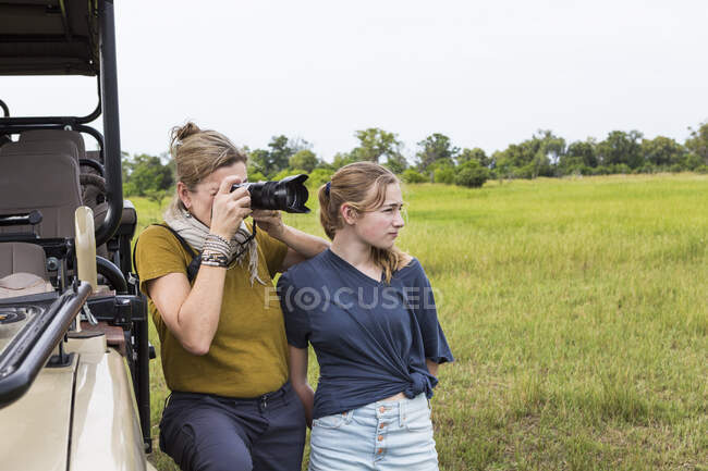 Mother photographing with teen daughter near safari vehicle, Botswana — Stock Photo