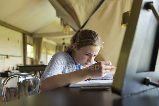 Chica de 13 años escribiendo en su diario, campamento de tiendas de campaña, Botswana - foto de stock
