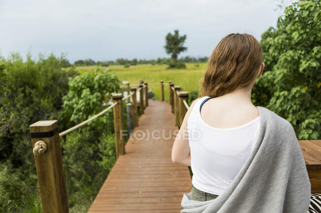 Vista traseira da menina de 13 anos andando em um caminho de madeira em um acampamento em safari — Fotografia de Stock
