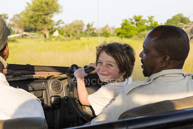 Sorridente 6 anni ragazzo sterzo safari veicolo, Botswana — Foto stock