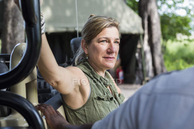 Retrato de mujer adulta apoyada en vehículo safari, campamento de tiendas de campaña, Botsuana - foto de stock