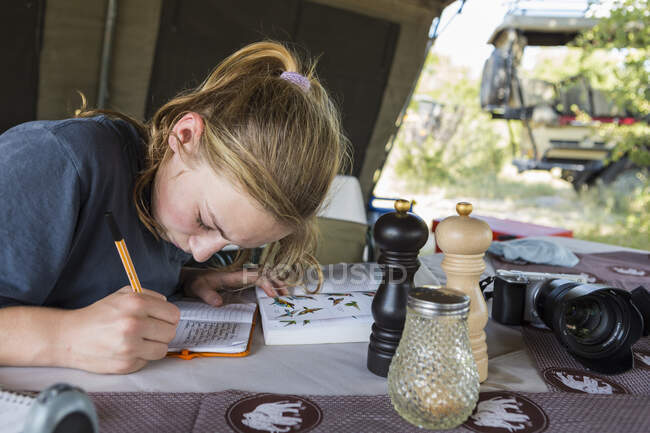 Una adolescente escribiendo en su diario en una tienda de campaña. - foto de stock