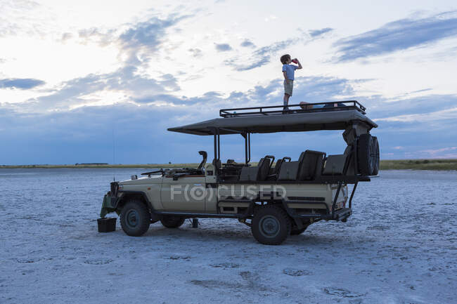 6-летний мальчик стоит на вершине автомобиля сафари, Nxai Pan, Ботсвана — стоковое фото