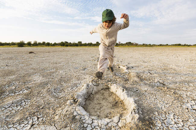 6 year old boy leaping into elephant footprints, Nxai Pan, Botswana — Stock Photo