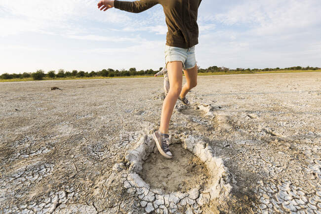 13 year old girl leaping into elephant footprints, Nxai Pan, Botswana — Stock Photo