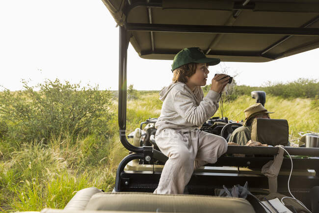 Niño de 6 años con prismáticos en vehículo safari, Botswana - foto de stock