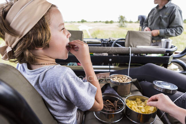 6-jähriger Junge isst Snacks im Safarifahrzeug, Botswana — Stockfoto