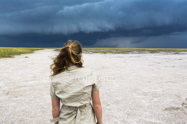 Rear view of 13 year old girl looking at dramatic sky, Nxai Pan, Botswana — Stock Photo