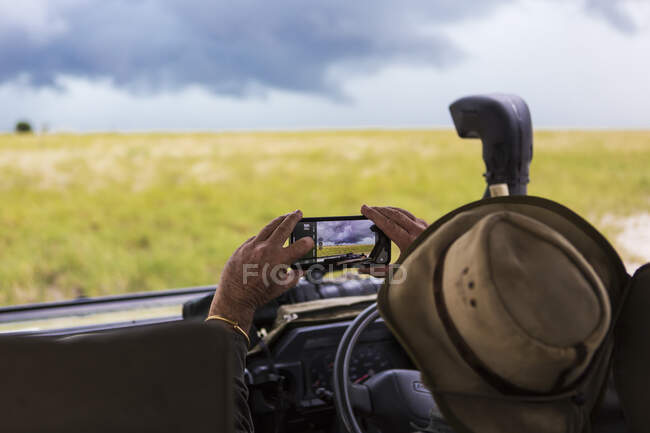 Safari guide taking smart phone picture of approaching storm clouds. — Stock Photo