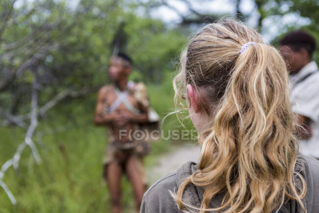 Rear view of teen girl walking with a group of bushmen from the San people. — Stock Photo