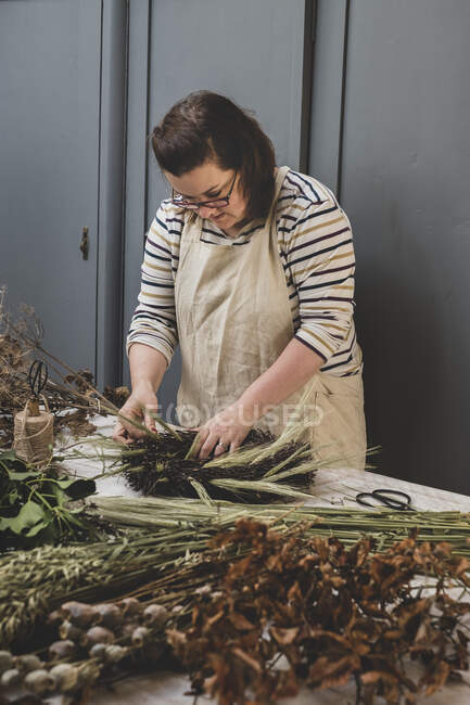 Woman making a winter wreath, adding dried grasses and seedheads and twigs with brown leaves. — Stock Photo