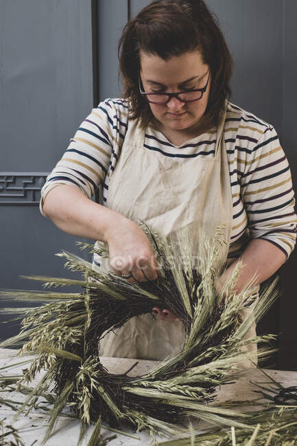 Donna che fa una ghirlanda invernale, aggiungendo erbe secche e teste di semenzaio e ramoscelli con foglie marroni. — Foto stock