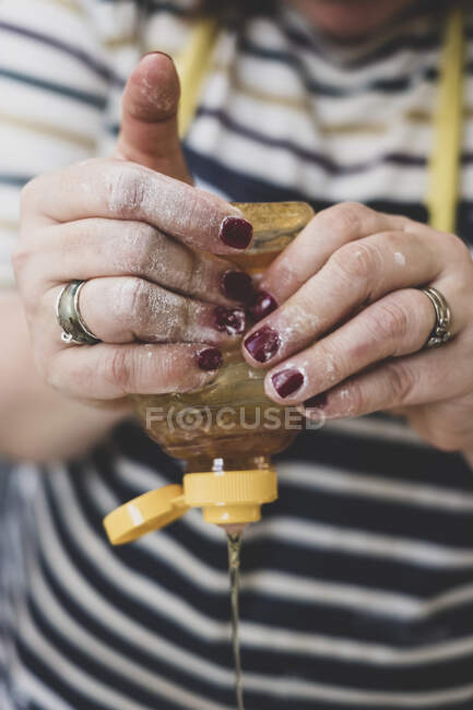 Mãos apertando mel de uma garrafa de plástico — Fotografia de Stock