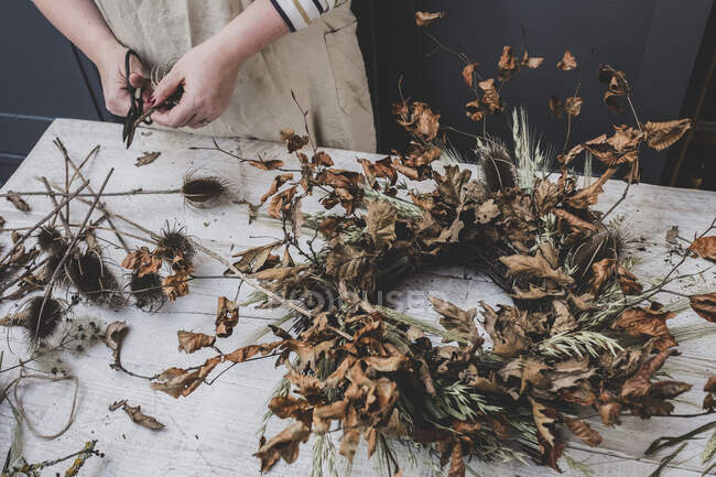 Woman making a small winter wreath of dried plants, brown leaves and twigs, and seedheads. — Stock Photo