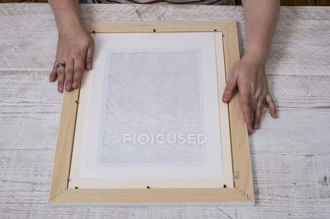 Persona que ajusta un marco de imagen alrededor de una impresión. - foto de stock