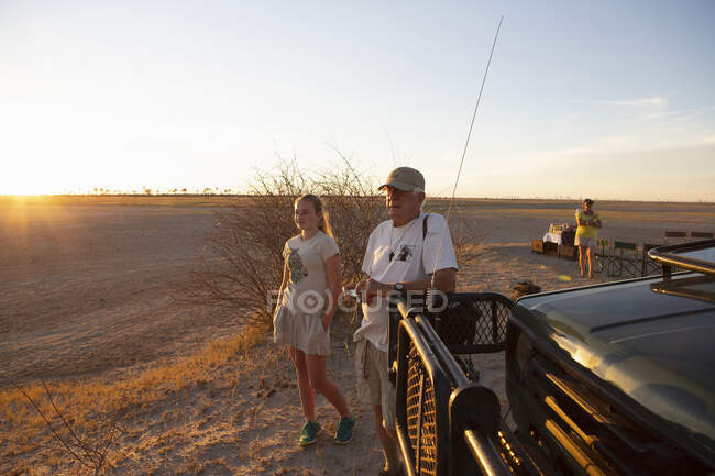 Abuelo y nieta mirando hacia el atardecer en el desierto de Kalahari - foto de stock