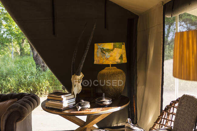 L'interno di una tenda in un campo safari con lampada elettrica e tavolo, sedie e divano, lati della tenda arrotolati. — Foto stock