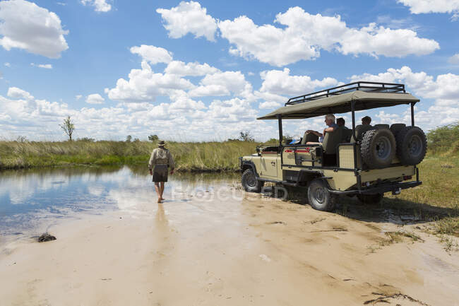 Un véhicule safari avec passagers, et un guide marchant à travers le sable — Photo de stock