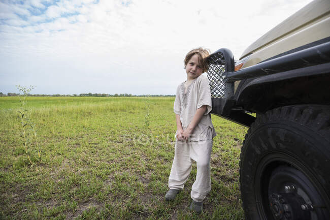 Niño de 6 años apoyado en vehículo safari, Botswana - foto de stock