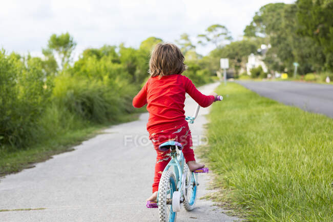 Un niño de cinco años con una camisa roja montando su bicicleta en una tranquila calle residencial. - foto de stock