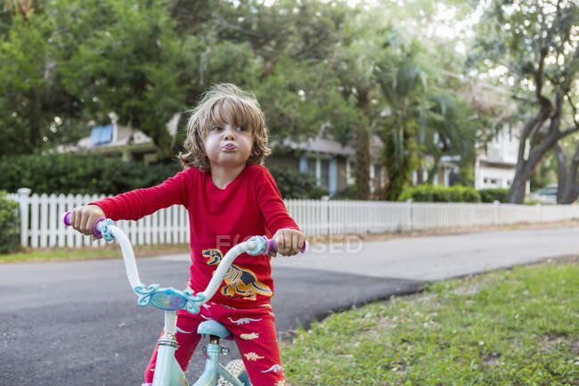 Un garçon de cinq ans en chemise rouge sur son vélo dans une rue résidentielle calme. — Photo de stock