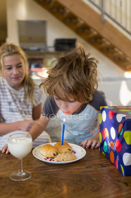 5 year old boy blowing out candle on croissant — Stock Photo
