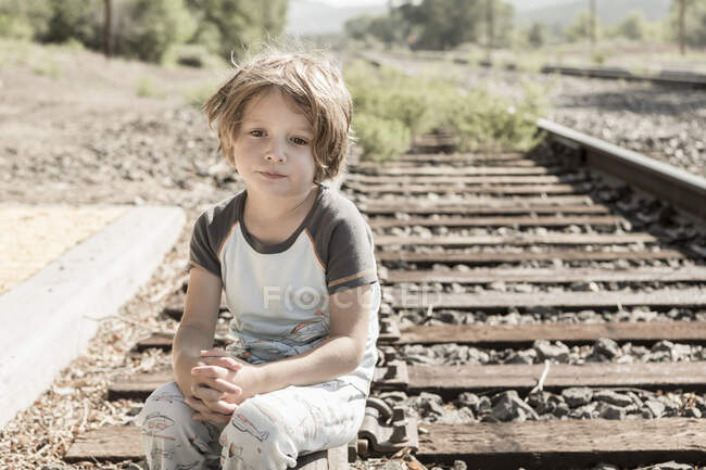 5 year old boy sitting on railroad tracks — Stock Photo