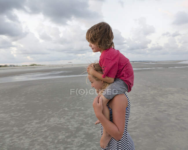 Пятилетний брат катается на плечах сестры на пляже, Джорджия — стоковое фото
